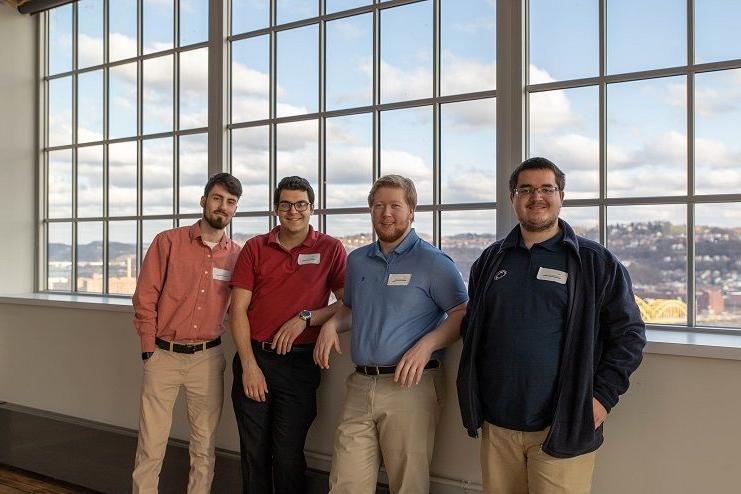 Four male students stand by window